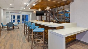 A modern bar area with a white countertop, blue bar stools, and a wooden accent wall. - Hampton Inn Cape Cod Canal (Buzzards Bay)