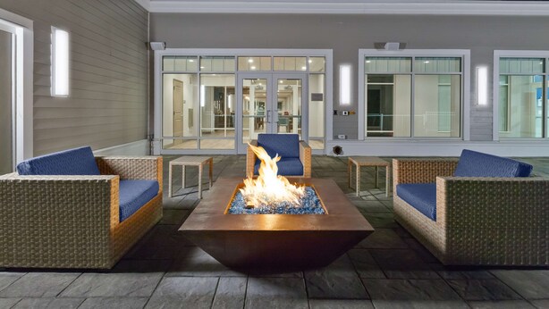 A fire pit surrounded by wicker furniture with blue cushions, set on a stone patio. - Hampton Inn Cape Cod Canal (Buzzards Bay)