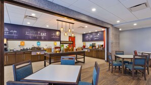A restaurant with a modern interior, featuring a counter with food displays, seating areas with tables and chairs, and overhead lighting. - Hampton Inn Cape Cod Canal (Buzzards Bay)