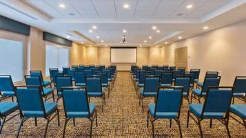 A conference room with rows of blue chairs, a projector screen, and a carpeted floor.