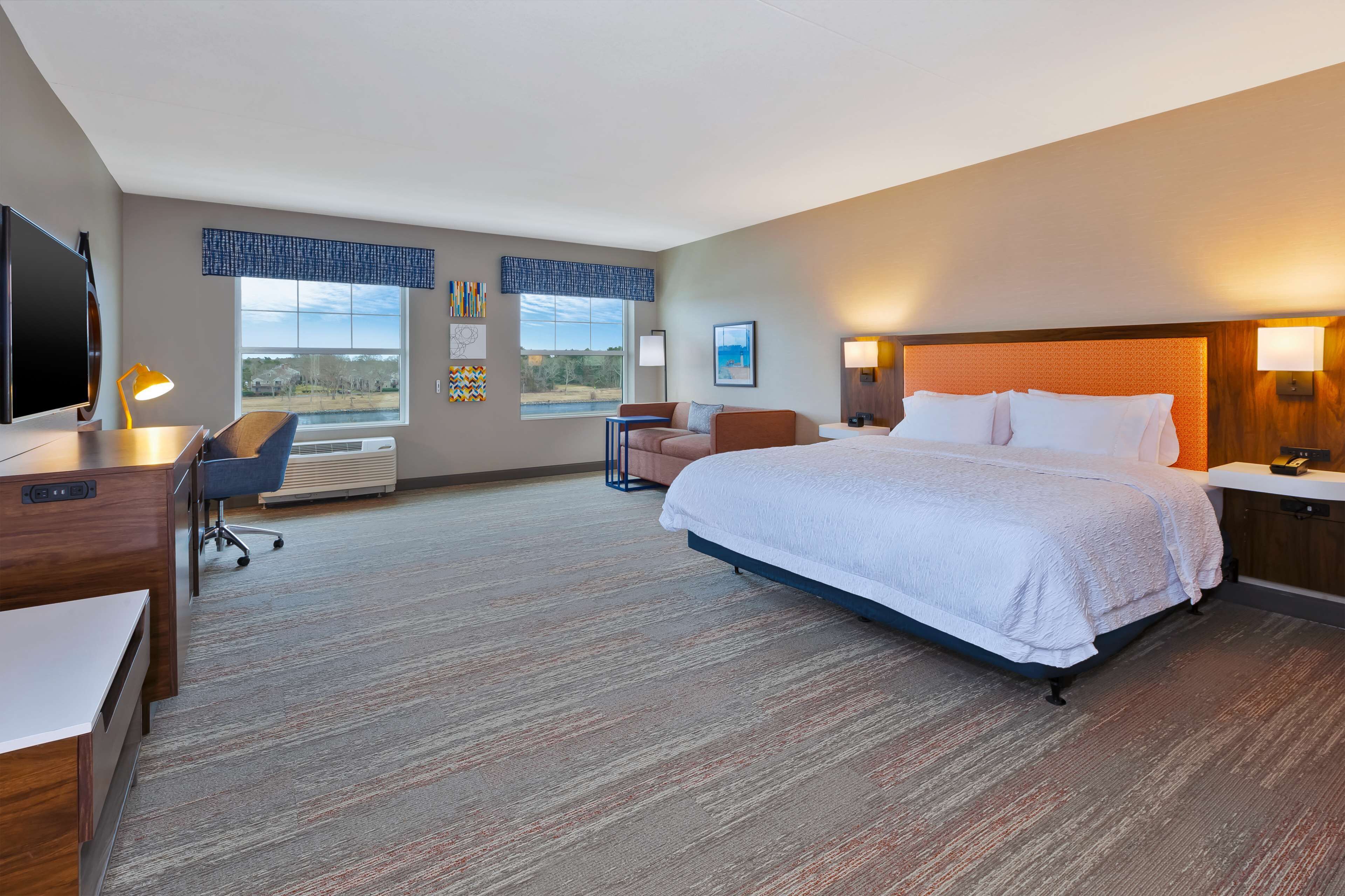 A hotel room with a large bed, a desk with a chair, a TV, and a window with a view of the outdoors.