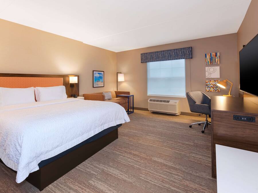 Quarto de hotel com uma cama grande, uma escrivaninha, uma cadeira, uma TV e uma janela.