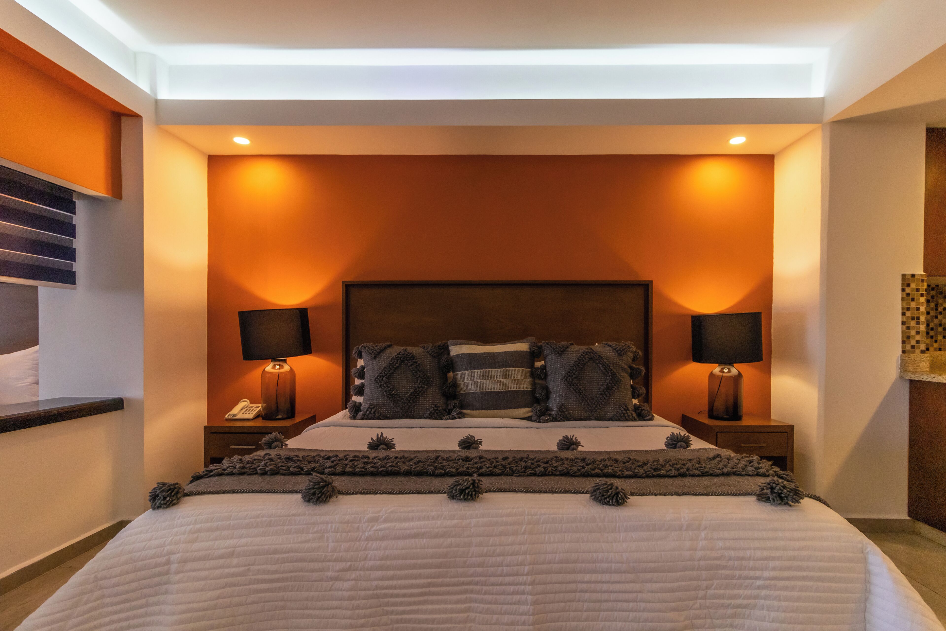 Une chambre à coucher moderne avec un grand lit, deux tables de chevet avec des lampes et une tête de lit dotée d’un éclairage intégré.