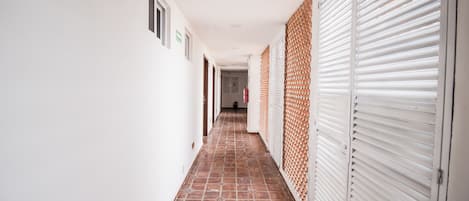 Un couloir doté d’un sol carrelé, de murs blancs et, d’un côté, de portes à persiennes fermées.