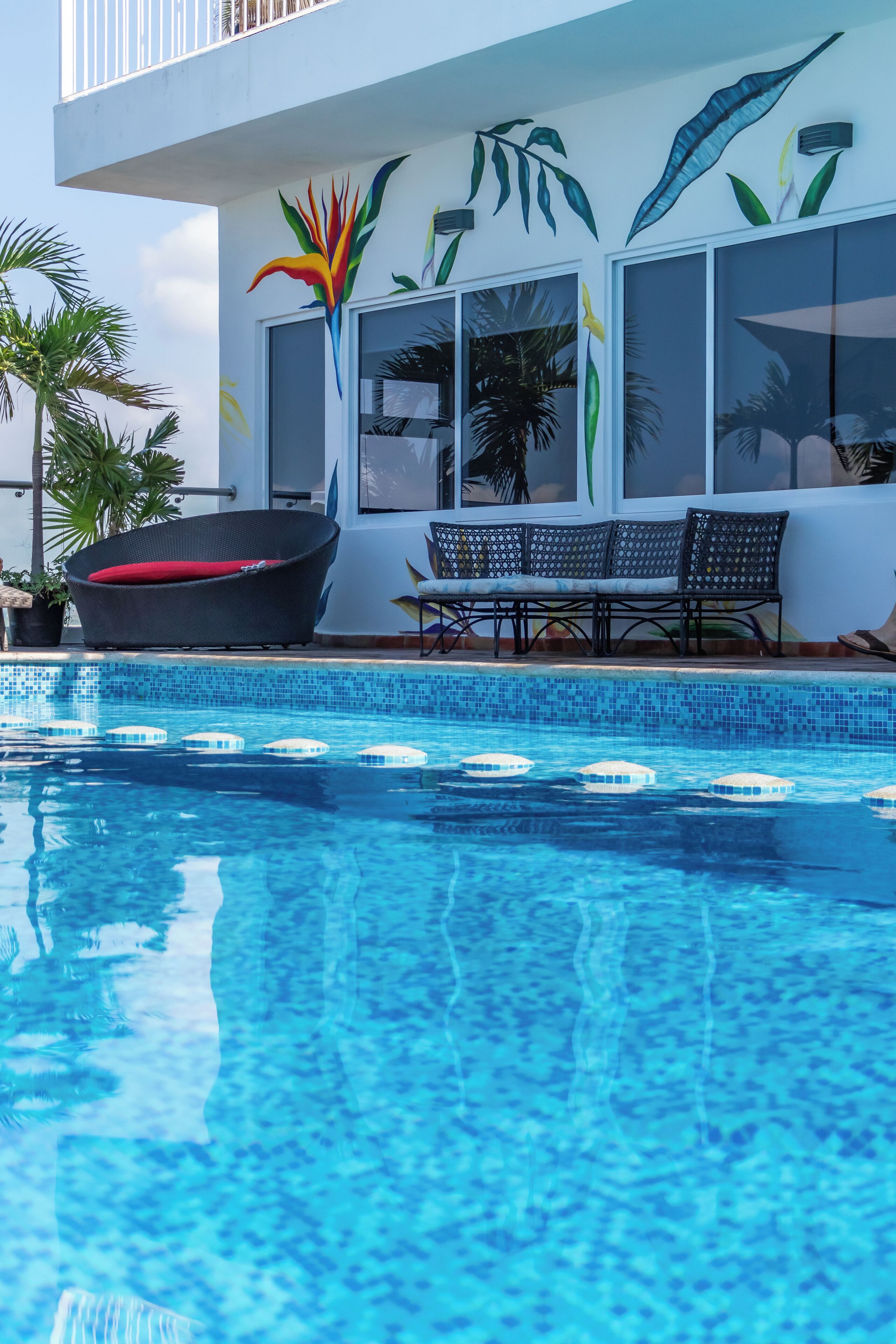 A swimming pool with lounge chairs and a wall with tropical leaf art.