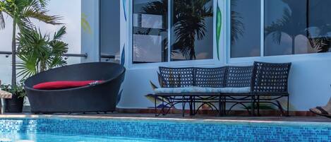 Une piscine dotée de chaises longues et d’un mur décoré de motifs représentant des feuilles tropicales.