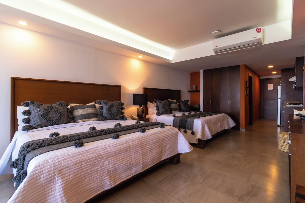A hotel room with two beds, a ceiling fan, and a kitchenette.