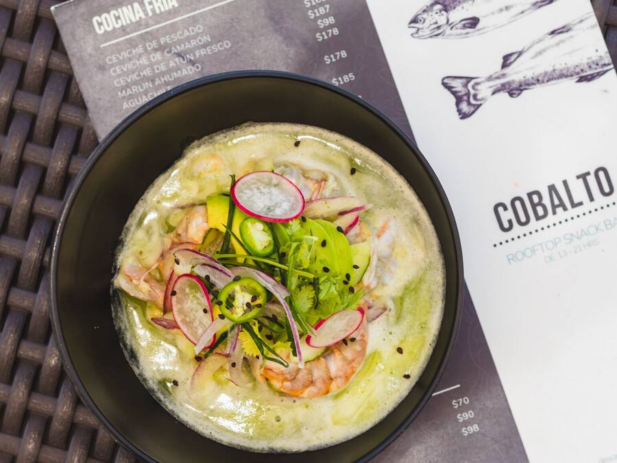 A bowl of seafood soup with shrimp, radishes, and greens, accompanied by a menu listing various dishes and prices.