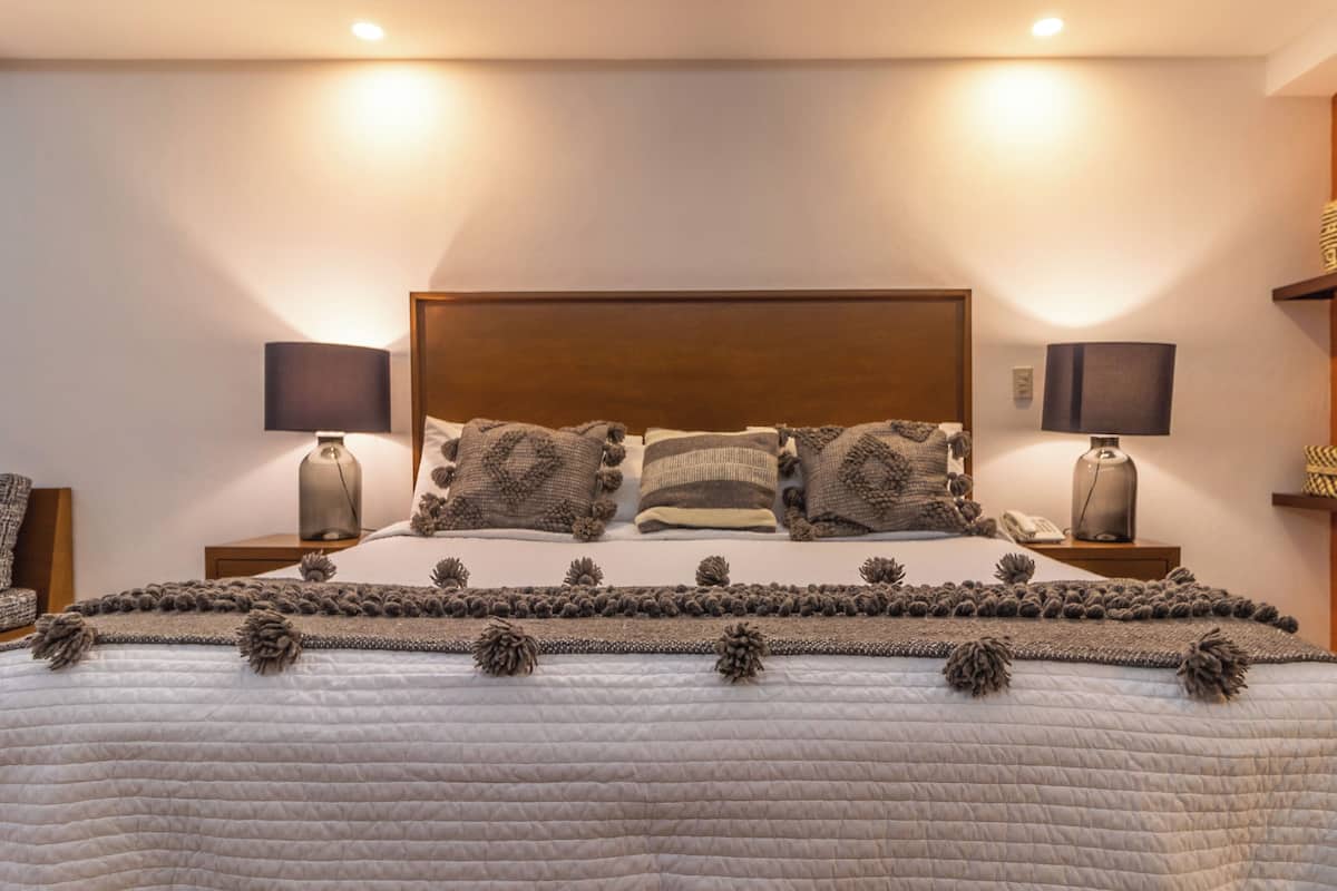 A neatly made bed with a patterned bedspread and decorative pillows, flanked by bedside tables with lamps and a phone.