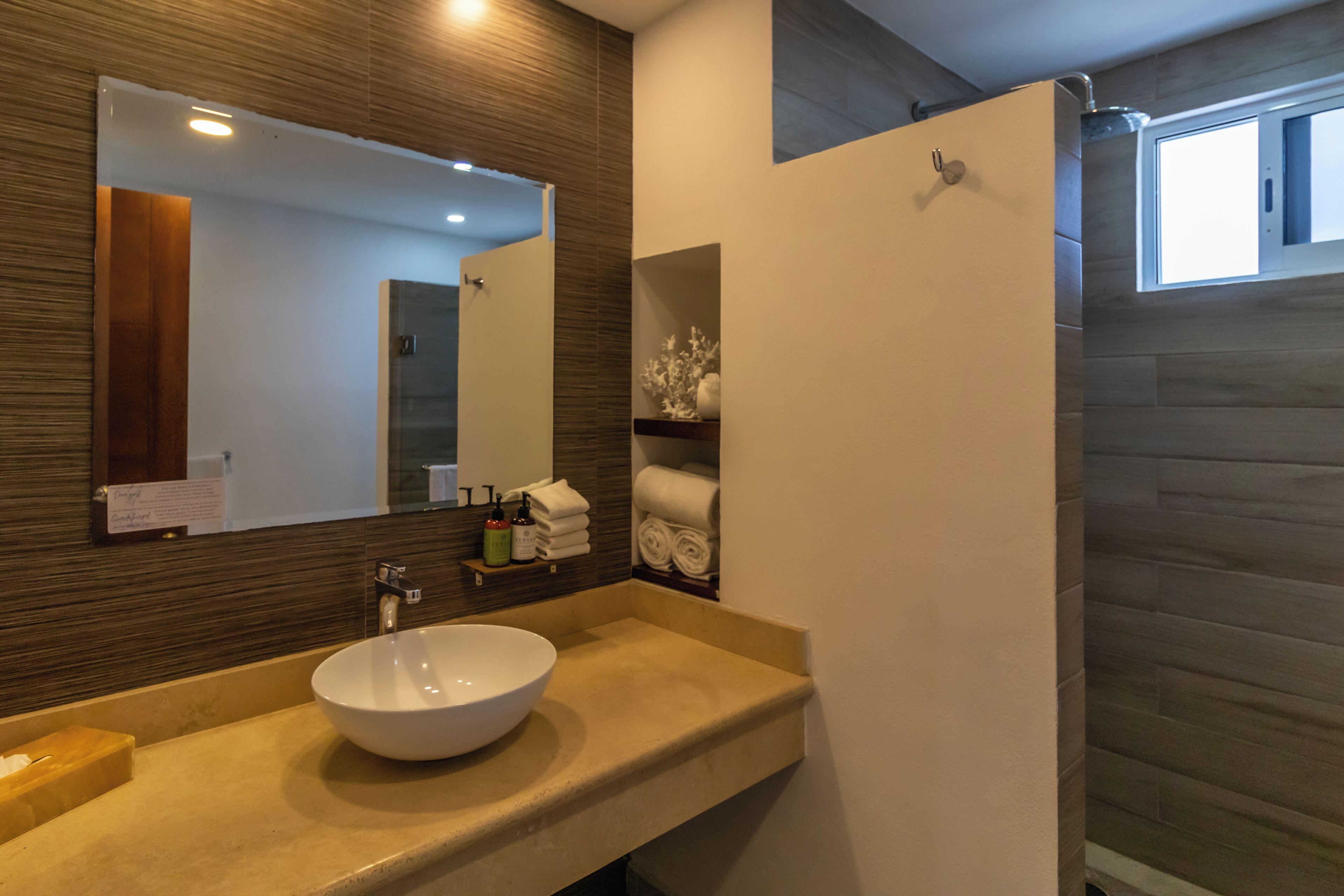 Un baño moderno con un espejo grande, un lavamanos color beige y un perchero para toallas.