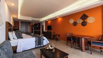 Quarto de hotel moderno com cama, sofá, mesa de jantar e cadeiras. Há uma TV na parede e uma pequena mesa com uma vela.