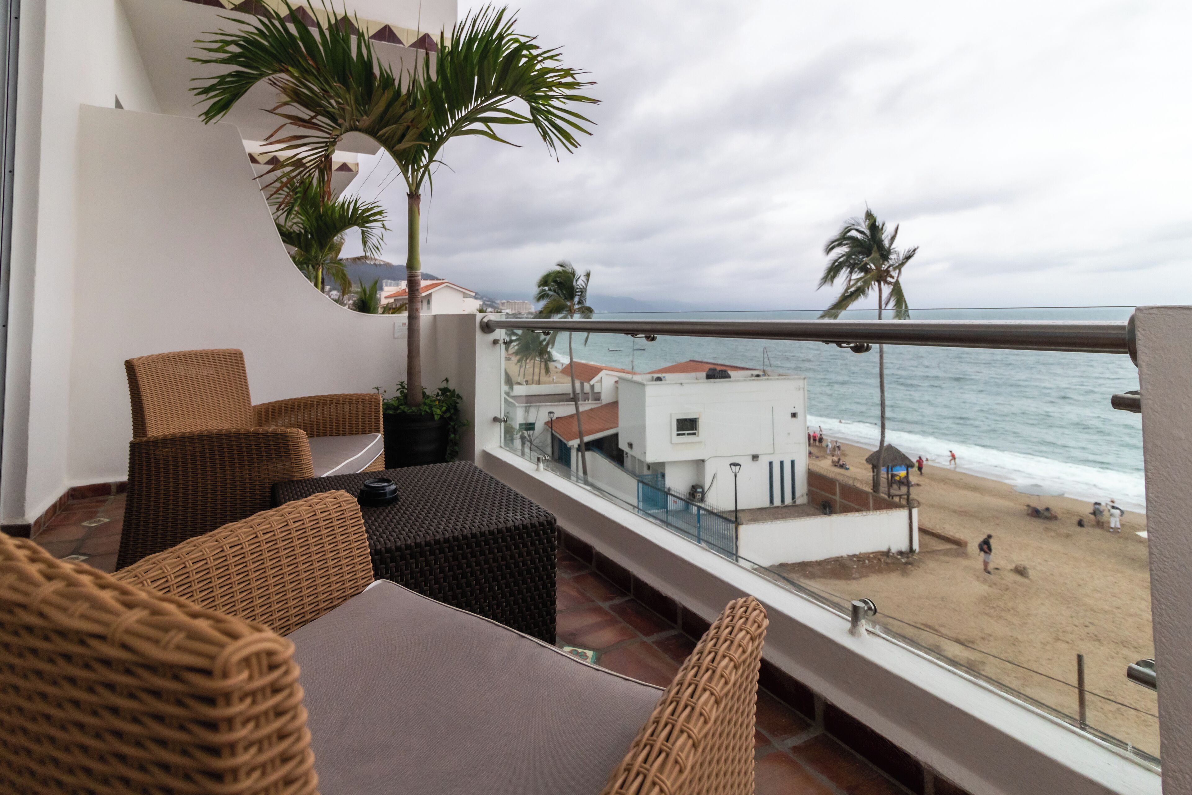 A balcony with wicker furniture, a view of the beach, and palm trees.
