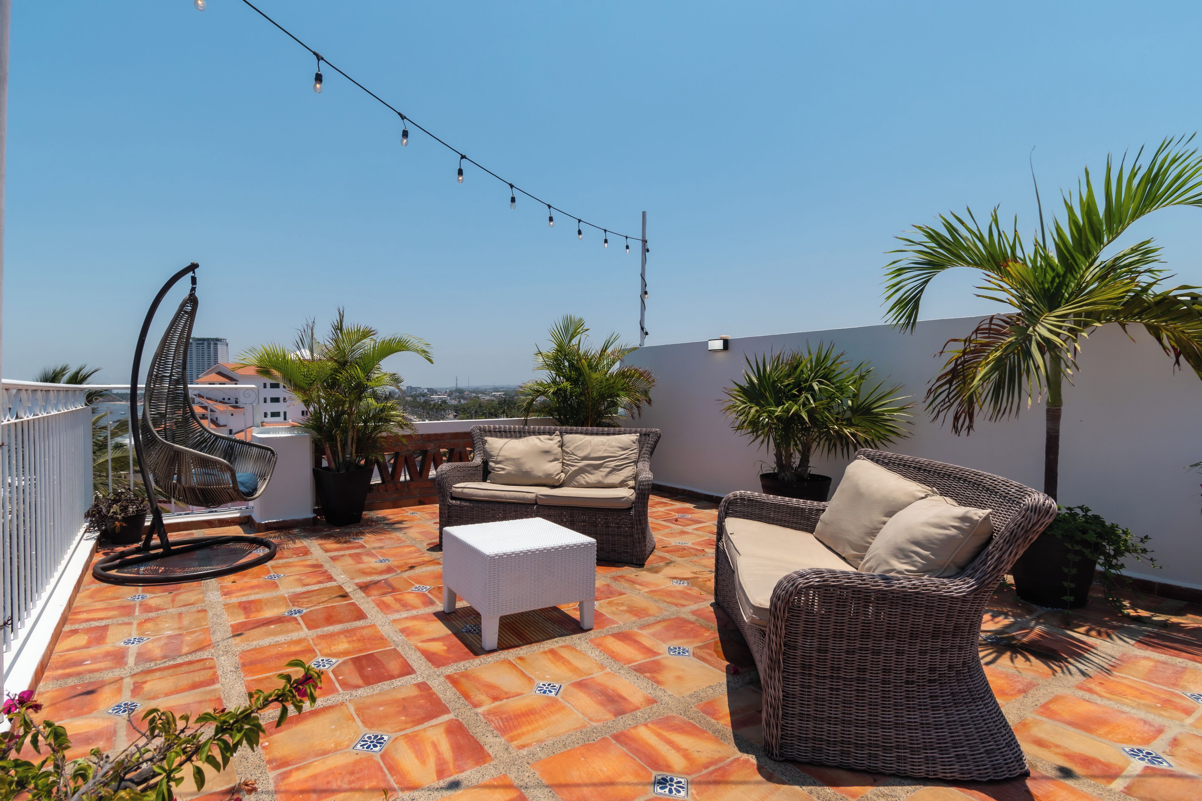 A rooftop terrace with wicker furniture, potted plants, and a string of lights.