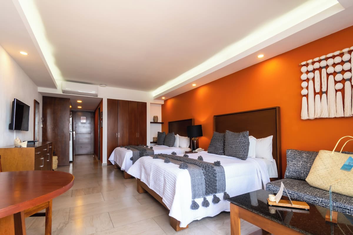 A hotel room with two beds, a sofa, a TV, and a dining table.