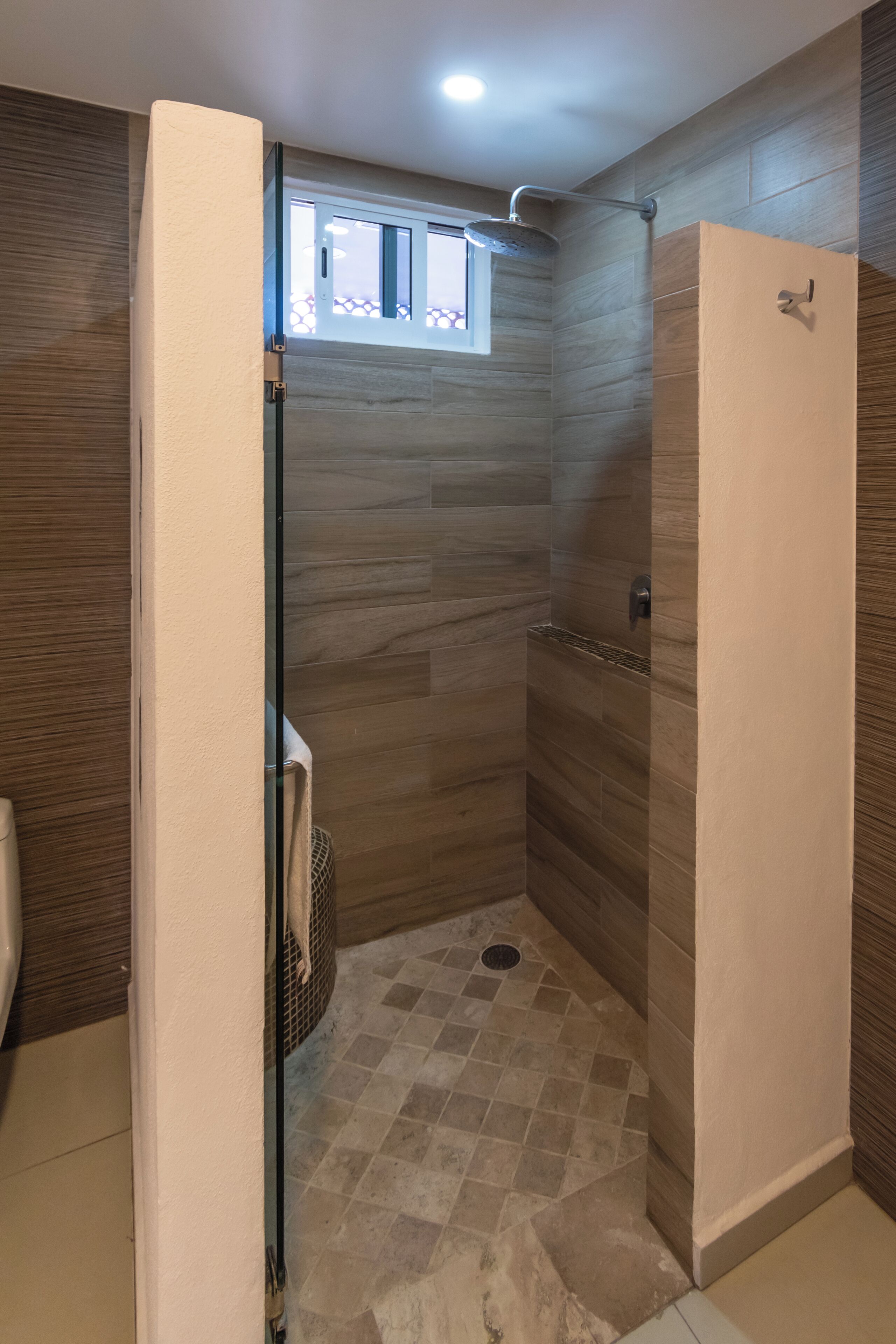 A modern bathroom with a shower, tiled floor, and a window above the shower.