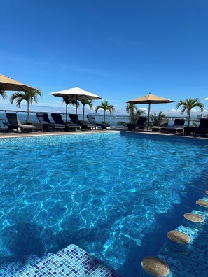 A clear blue pool with lounge chairs and umbrellas, surrounded by palm trees and a view of the ocean. - The Paramar Beachfront Boutique Hotel - Downtown Malecon (Puerto Vallarta)