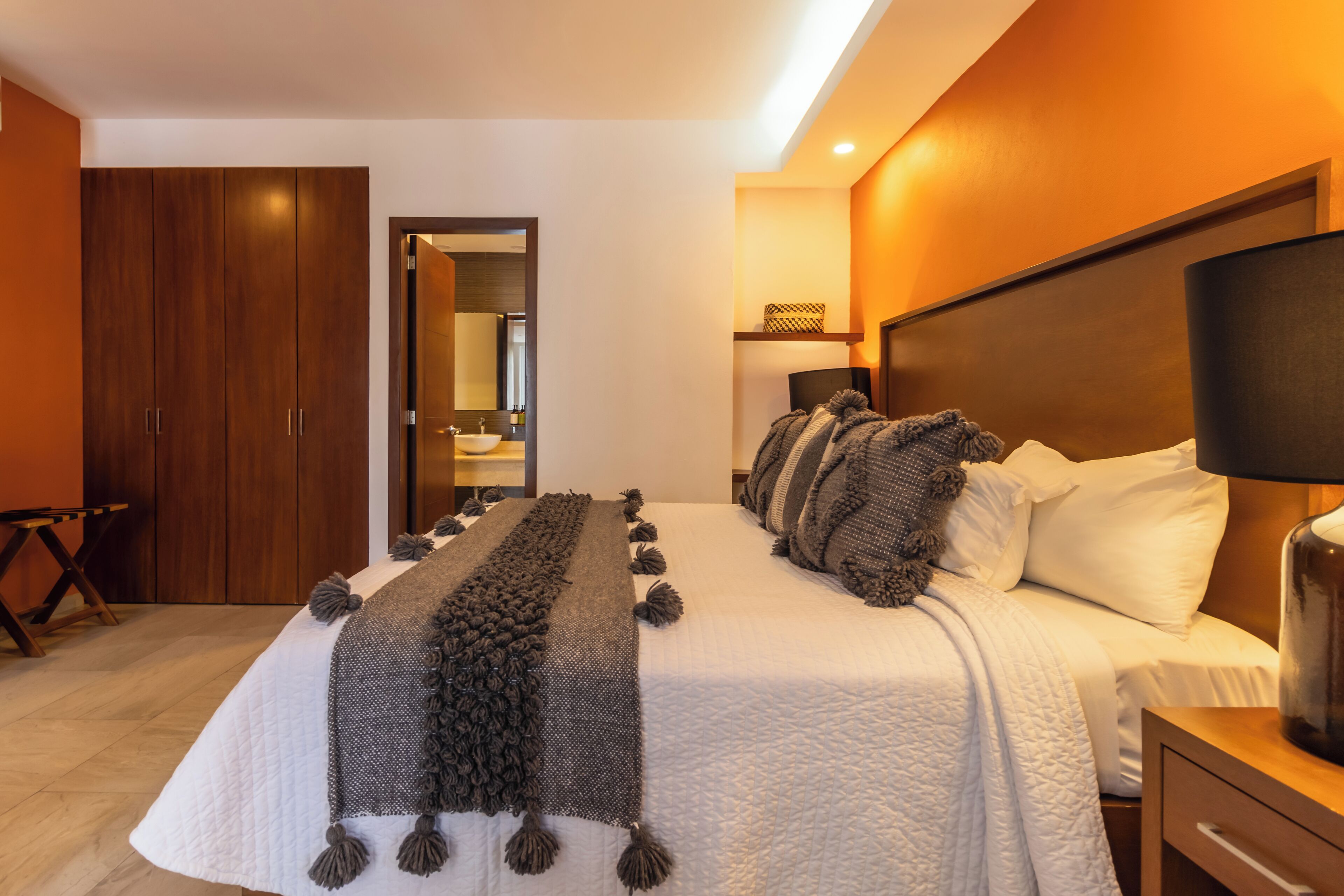 A hotel room with a large bed, a wooden wardrobe, a bedside table with a lamp, and a mirror above the bed.
