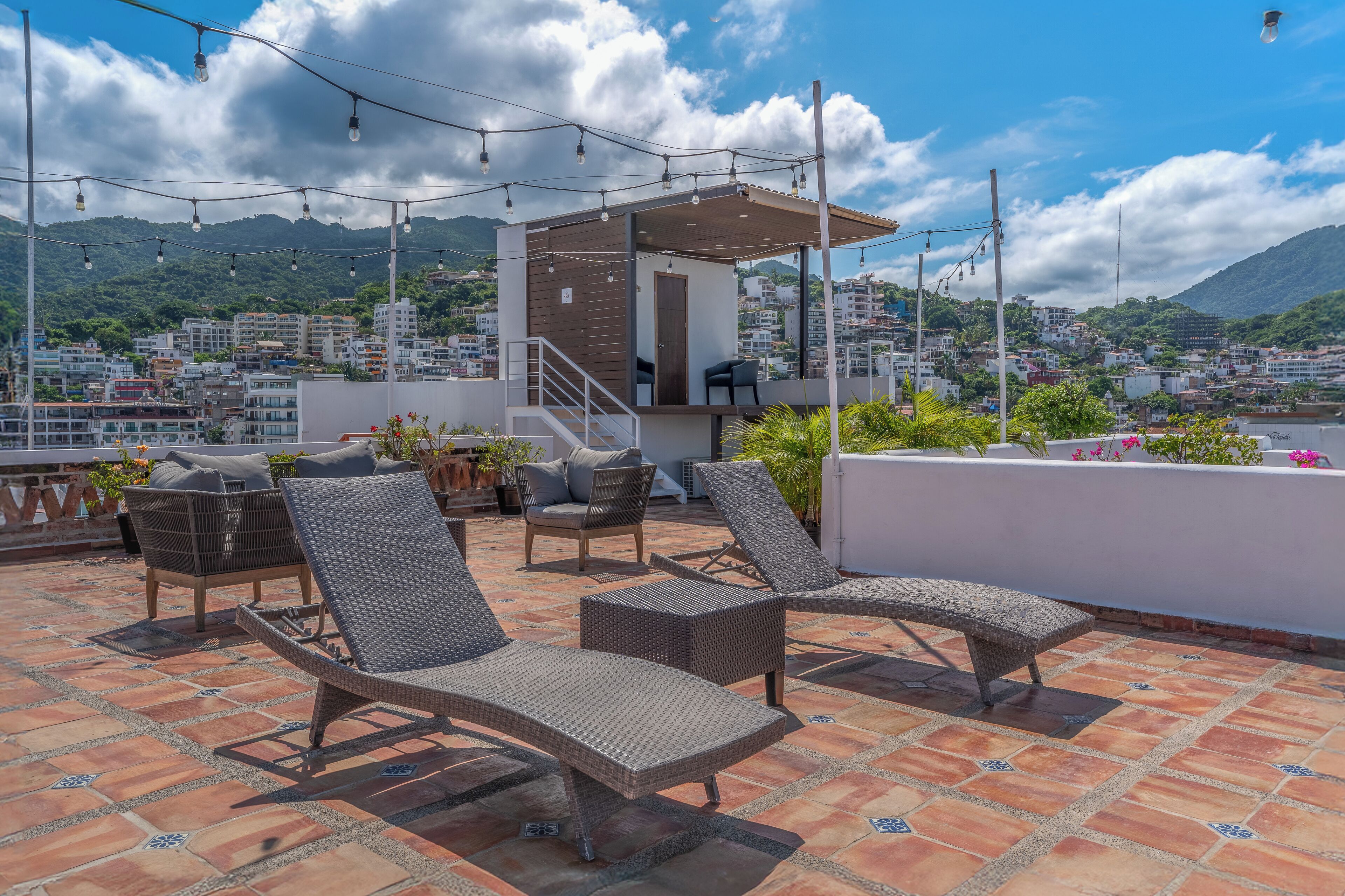 Terraza en la azotea con sillones de mimbre, un rincón cubierto para sentarse y vistas de un paisaje urbano con montañas al fondo.