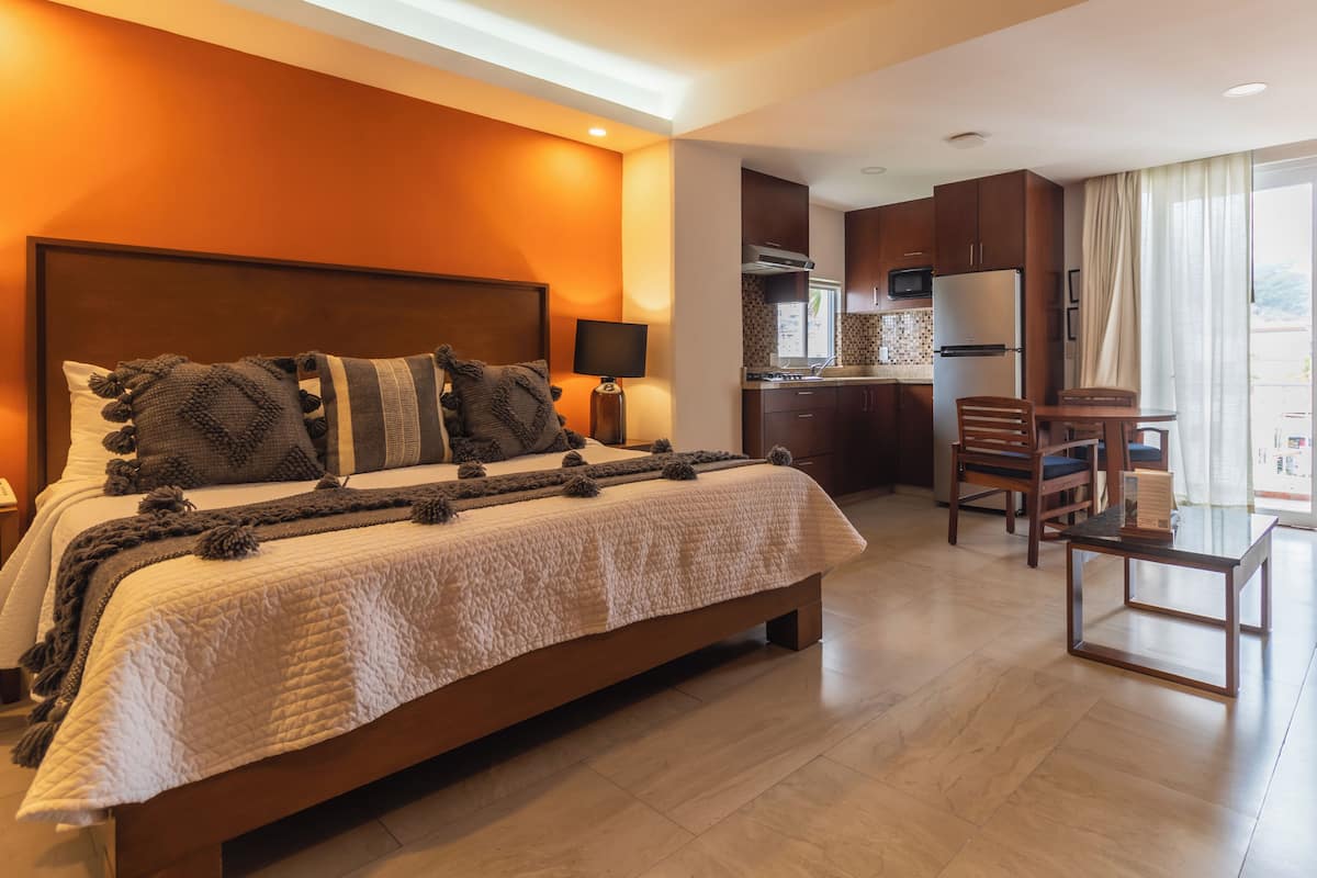 A hotel room with a large bed, a desk, and a kitchenette.