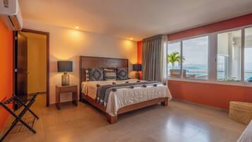 A bedroom with a bed, bedside tables, a lamp, a window with curtains, and a view of the ocean.