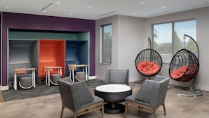 Une pièce moderne avec une table ronde et quatre chaises grises, un canapé avec des coussins orange et deux fauteuils suspendus noirs avec des coussins orange.