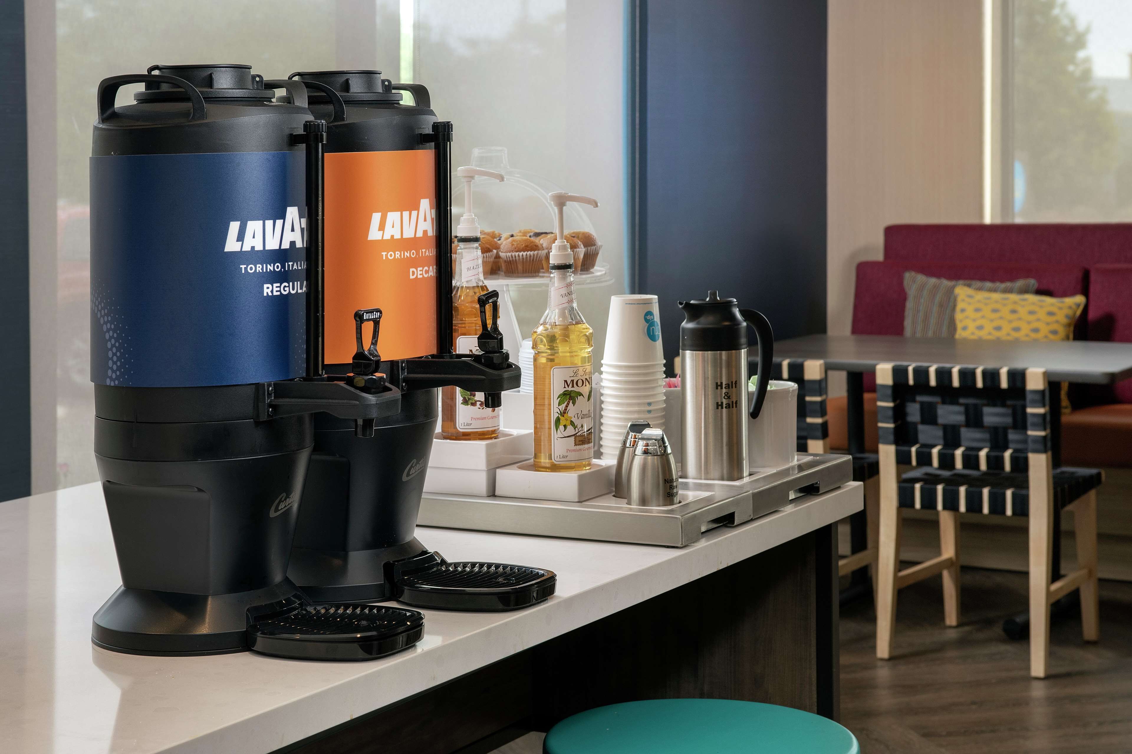 A coffee station with two coffee makers, a milk frother, and various coffee cups and bottles.