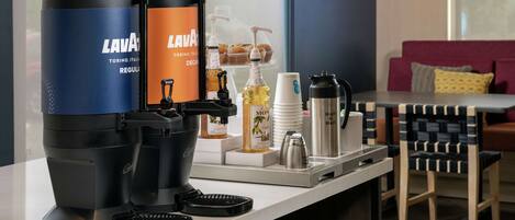 A coffee station with two coffee makers, a milk frother, and various coffee cups and bottles.