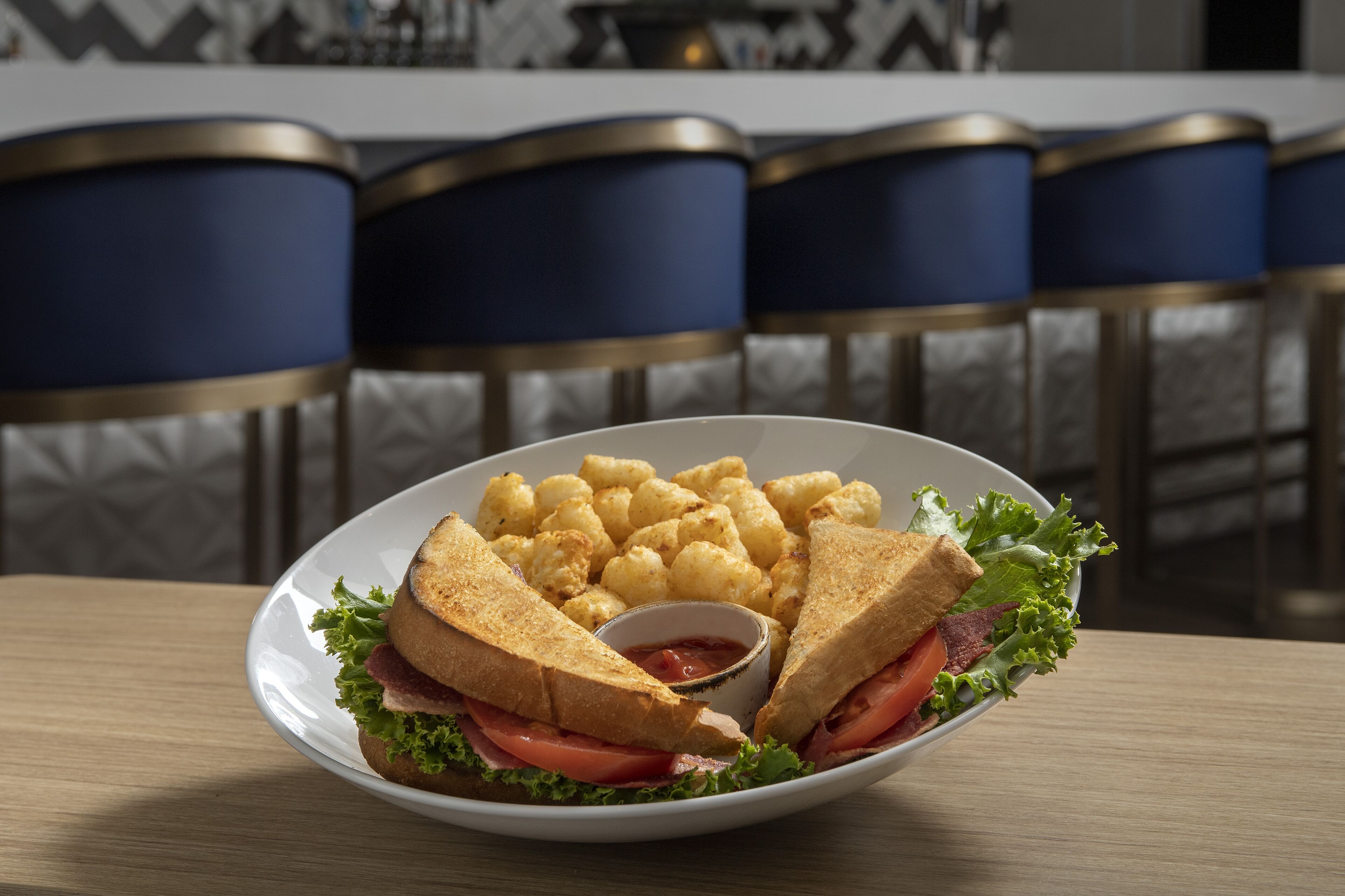 Ein Teller mit einem Sandwich, Pommes und einer kleinen Soße auf einem Tisch.