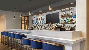 Un espace bar doté d’un long comptoir, de tabourets de bar bleus et d’étagères remplies de bouteilles.