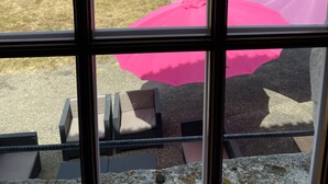 Udsigt gennem et vindue til en baghave med swimmingpool, havemøbler og parasoller.
