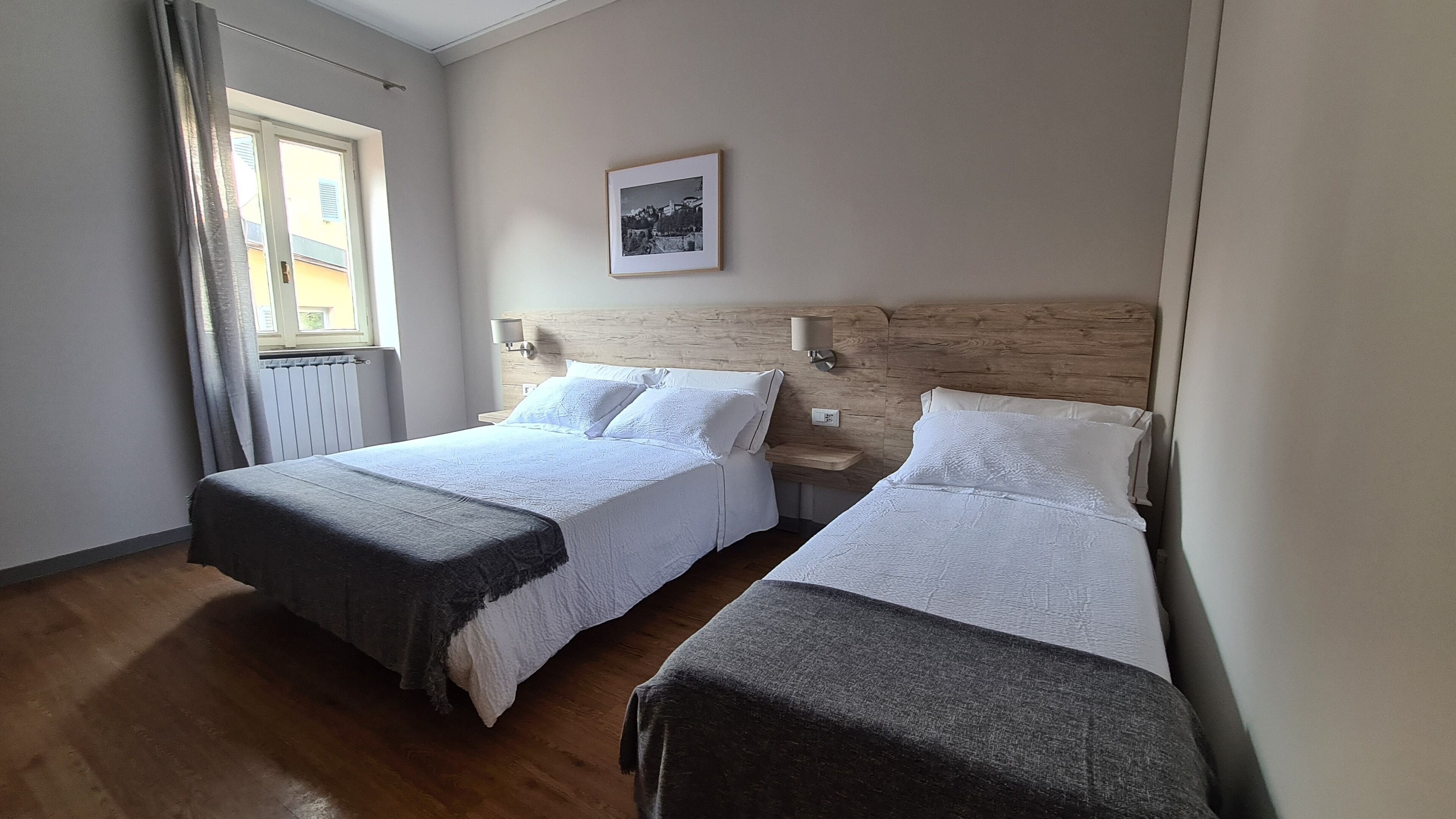 A hotel room with two beds, a window with curtains, a wall-mounted picture, and a wooden headboard.