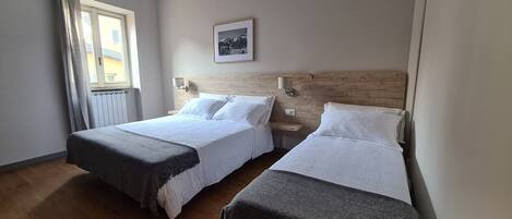 A hotel room with two beds, a window with curtains, a wall-mounted picture, and a wooden headboard.