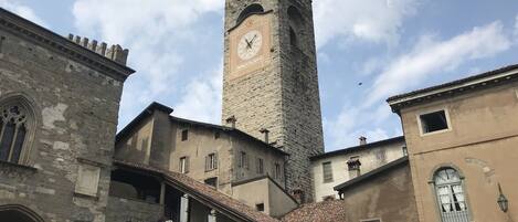 Un edificio histórico con una imponente torre de reloj, ventanas arqueadas y una escalera que conduce a un nivel superior.