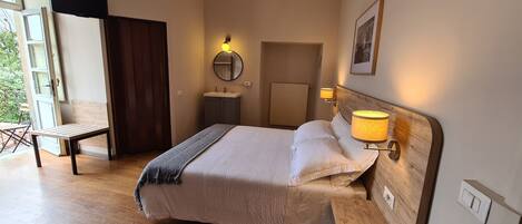 A bedroom with a bed, bedside lamps, a wooden headboard, a nightstand, a mirror, a window, and a door.