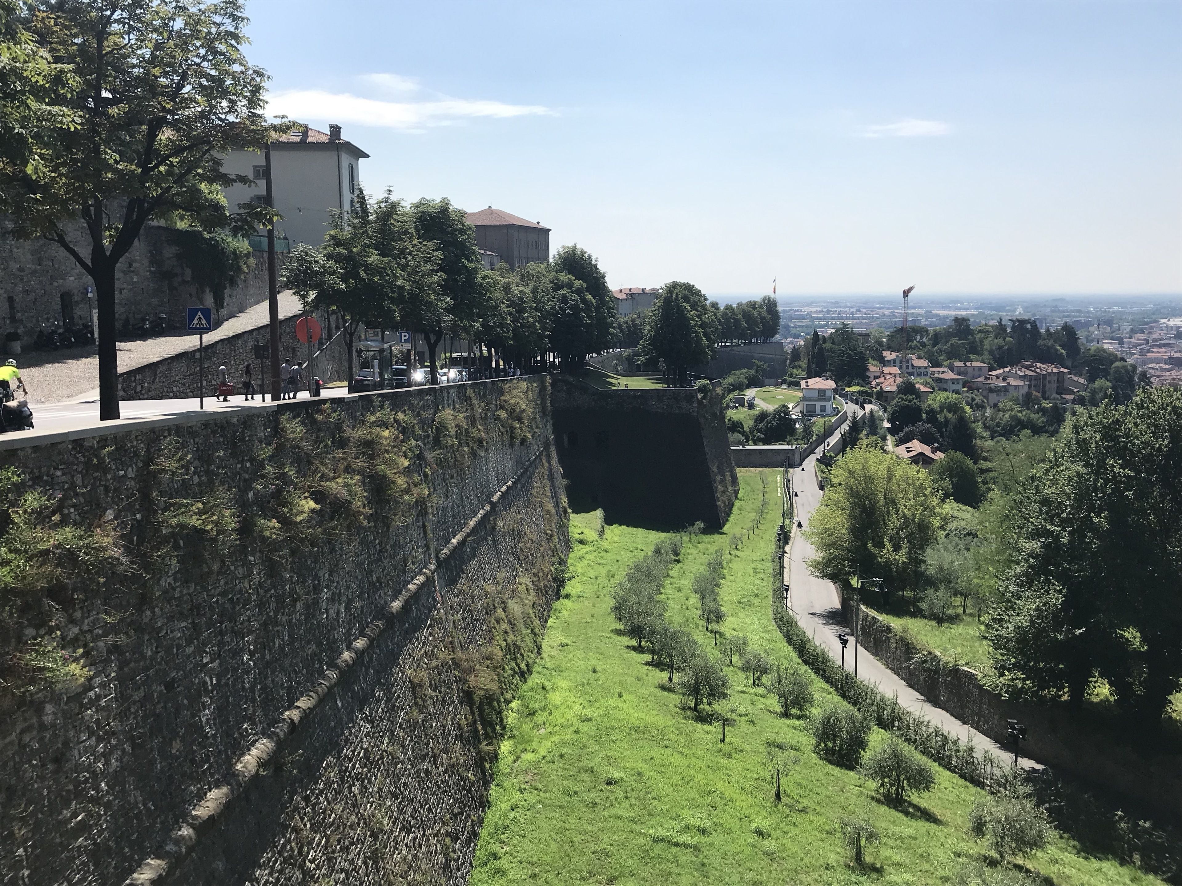 A stone wall with a steep drop, a paved path, and a view of a town below.
