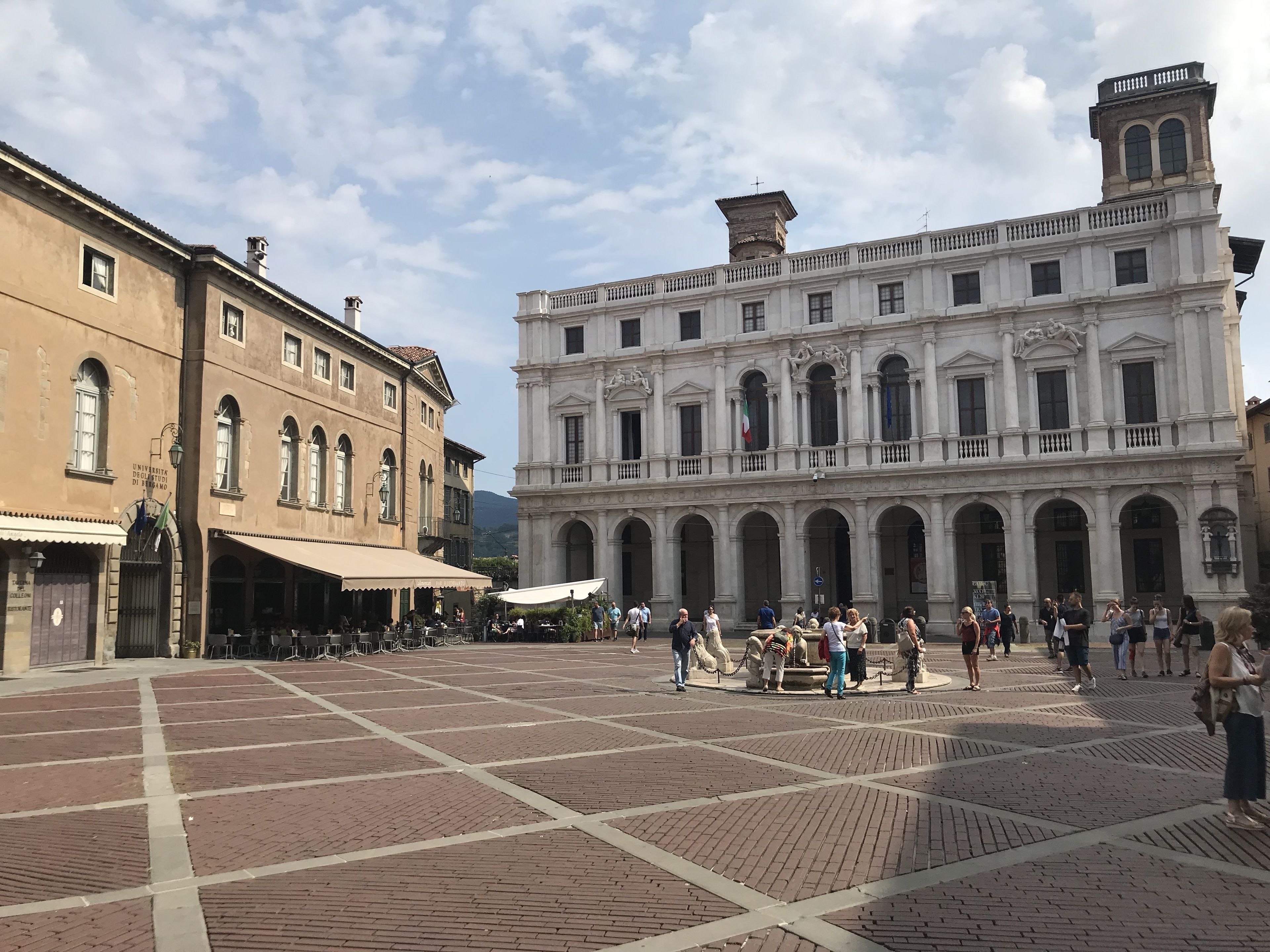 A spacious public square with a large white building featuring arched windows and a central fountain.