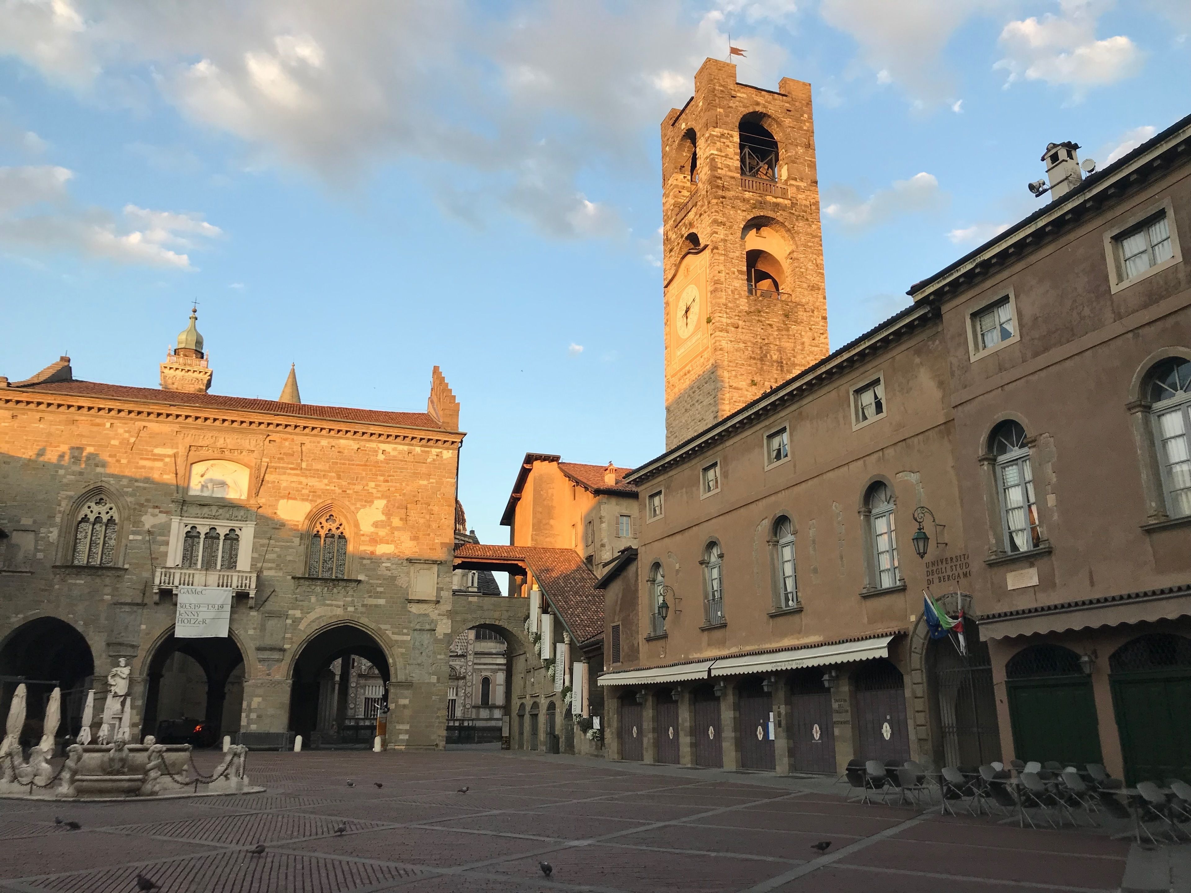 Ein historischer Platz mit einem markanten Turm, Steingebäuden und einem Brunnen.