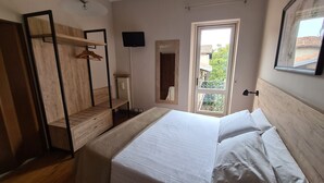 A bedroom with a bed, wooden wardrobe, a mirror, a TV, and a window with a view of greenery. - Il Sole Bergamo (Bergamo)
