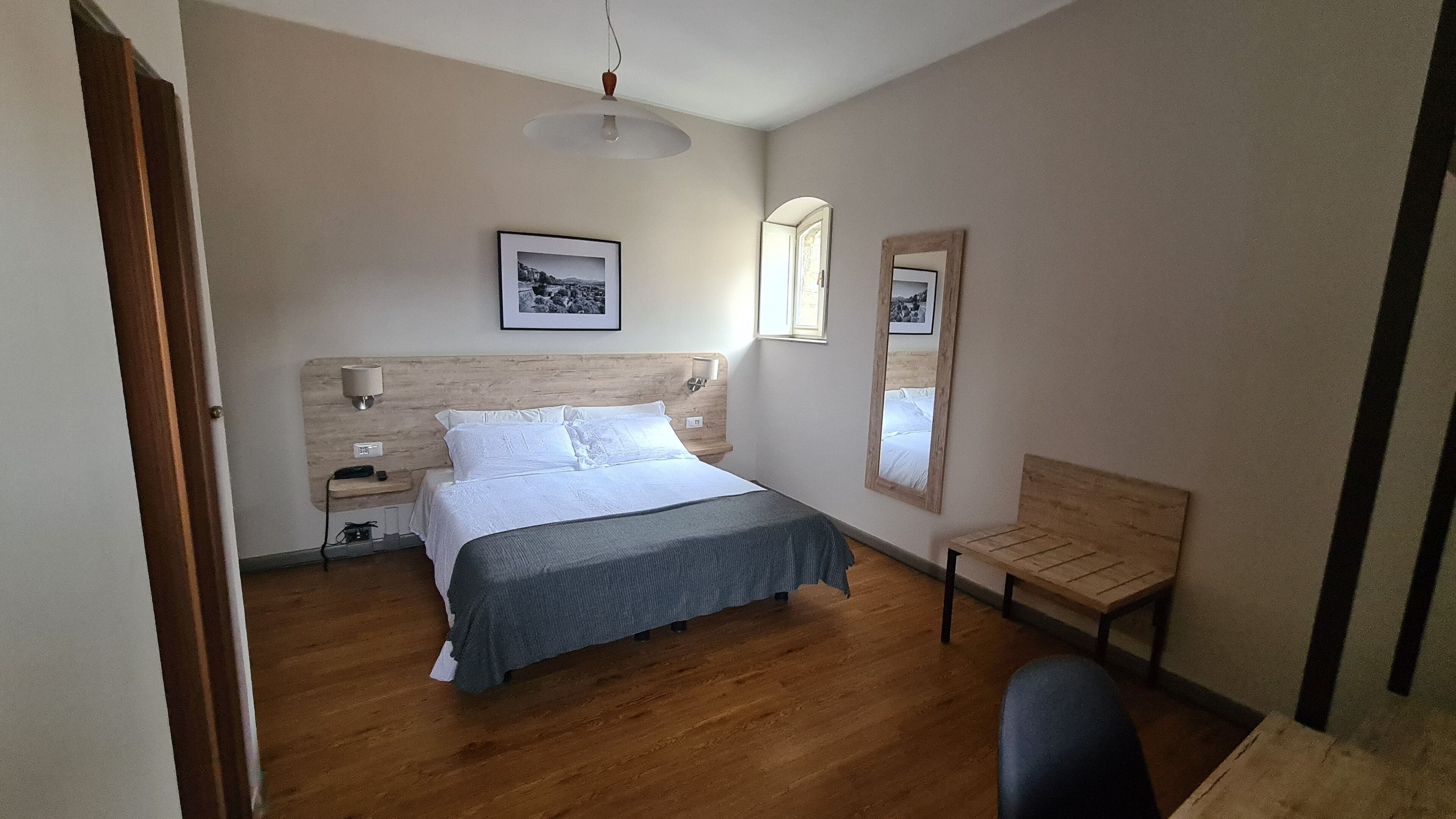 A bedroom with a bed, bedside tables, a lamp, a chair, a mirror, and a window.
