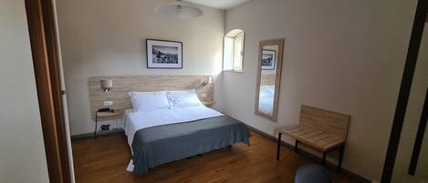 A bedroom with a bed, bedside tables, a lamp, a chair, a mirror, and a window.