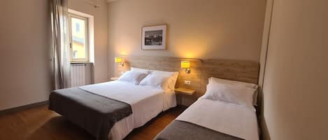 Habitación de hotel con dos camas, cabeceros de madera, lámparas de noche, un cuadro en la pared y una ventana con cortinas.