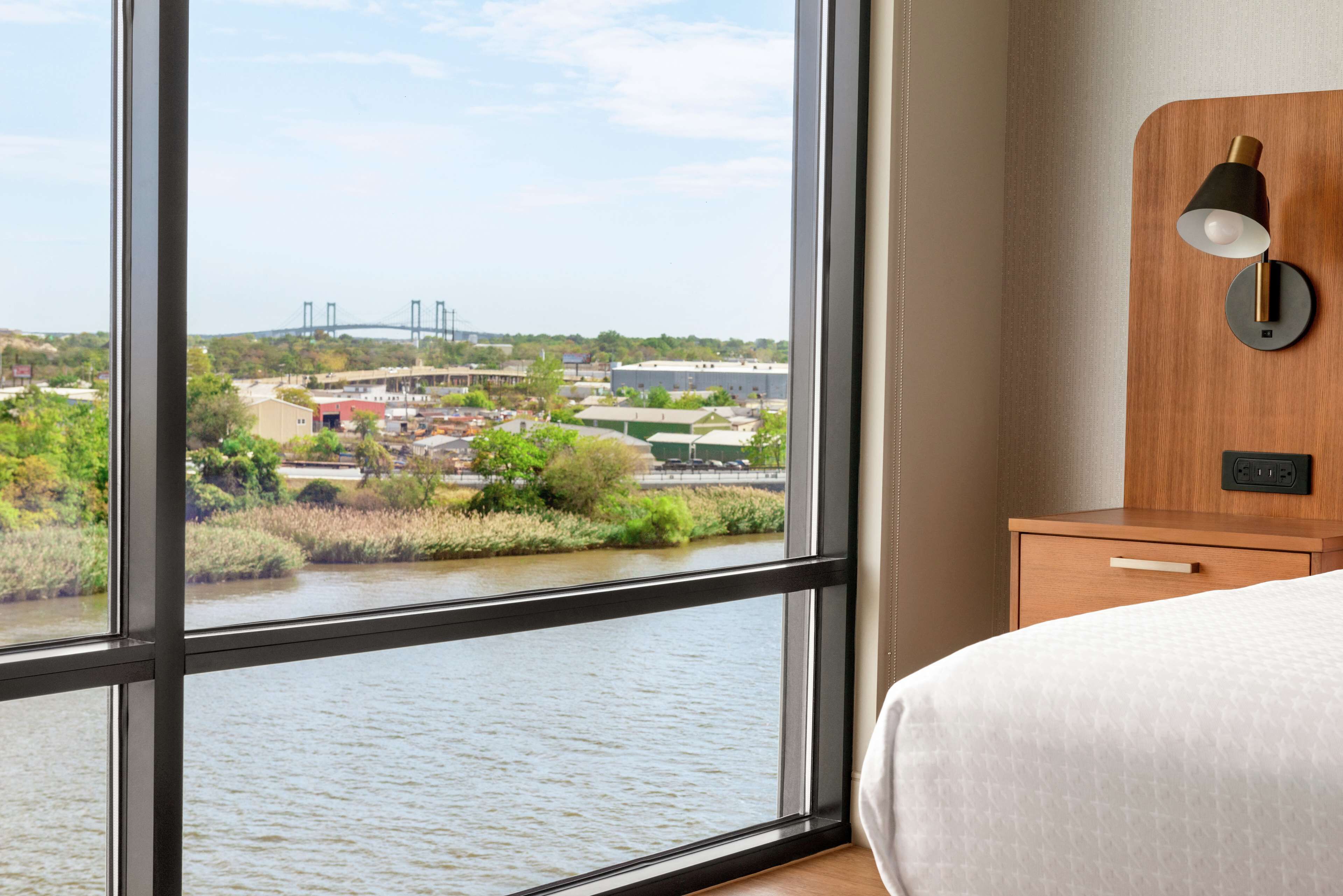 Une chambre d’hôtel dotée d’une grande fenêtre donnant sur une rivière et des bâtiments industriels.