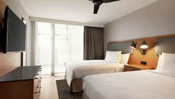 A hotel room with two beds, a flat-screen TV, a ceiling fan, and a large window with curtains.