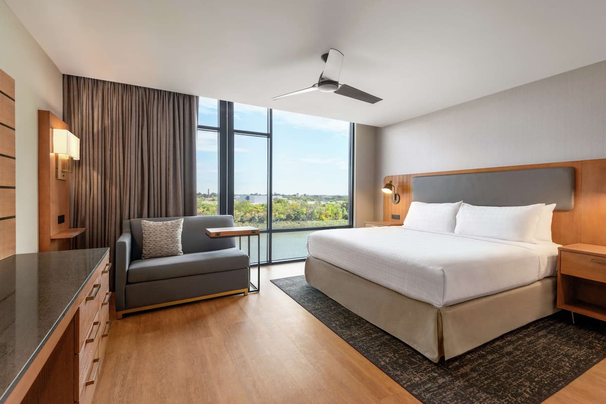 A modern hotel room with a large bed, a sofa, a desk, and a view of the city.