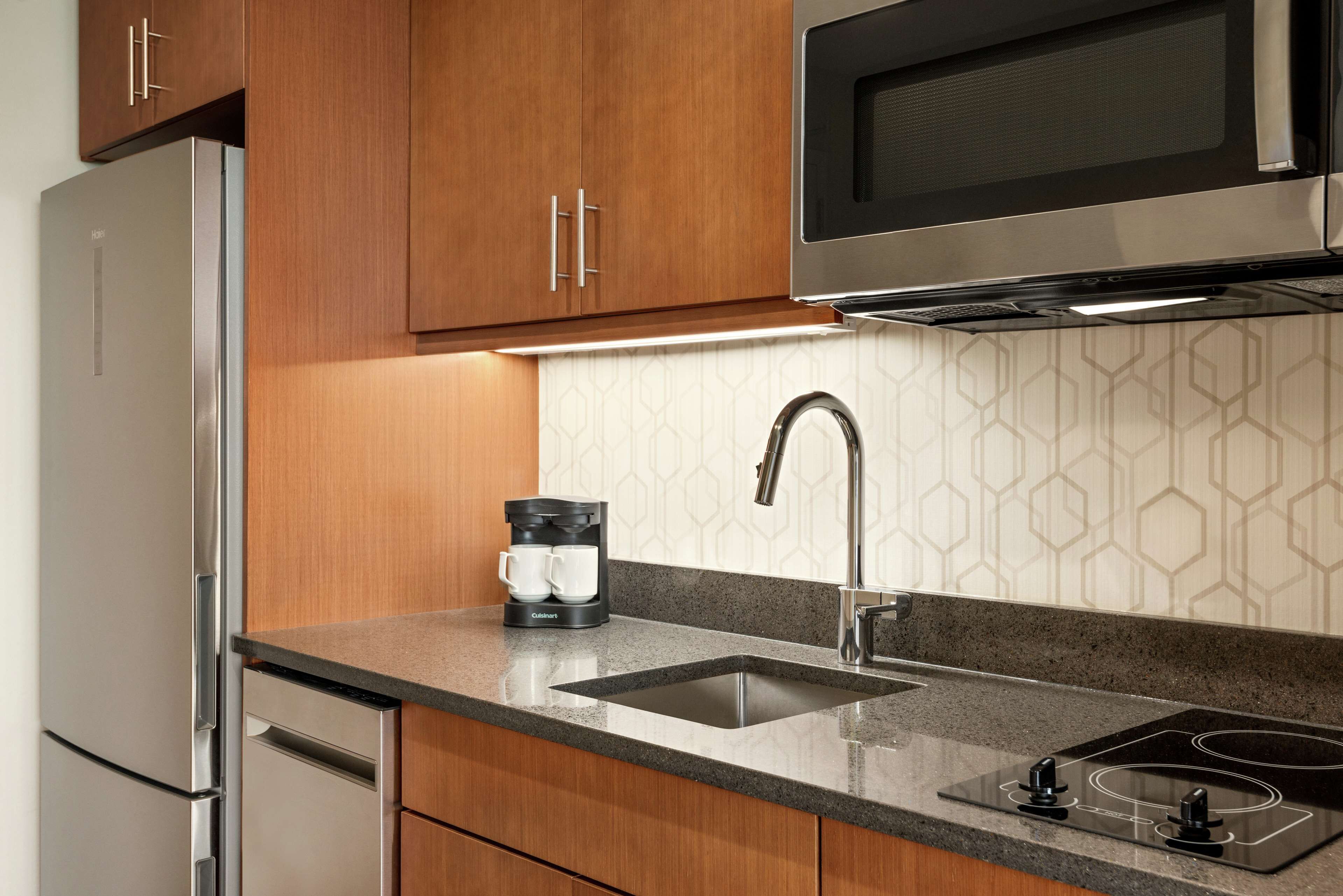 Una cocina con armarios de madera, un refrigerador de acero inoxidable, una cafetera, un lavamanos y un microondas.