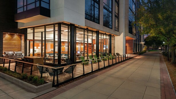 An outdoor dining area with tables and chairs, a grill, and a view of the interior through large windows. - Homewood Suites by Hilton Wilmington Downtown (Wilmington)