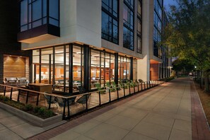 An outdoor dining area with tables and chairs, a grill, and a view of the interior through large windows. - Homewood Suites by Hilton Wilmington Downtown (Wilmington)