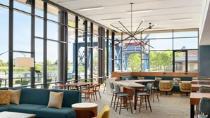 A modern restaurant with large windows, a blue sofa, yellow chairs, and a variety of seating options. - Homewood Suites by Hilton Wilmington Downtown (Wilmington)