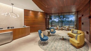 A modern hotel lobby with a wooden reception desk, blue and yellow seating, and large windows offering a view of the outdoors. - Homewood Suites by Hilton Wilmington Downtown (Wilmington)