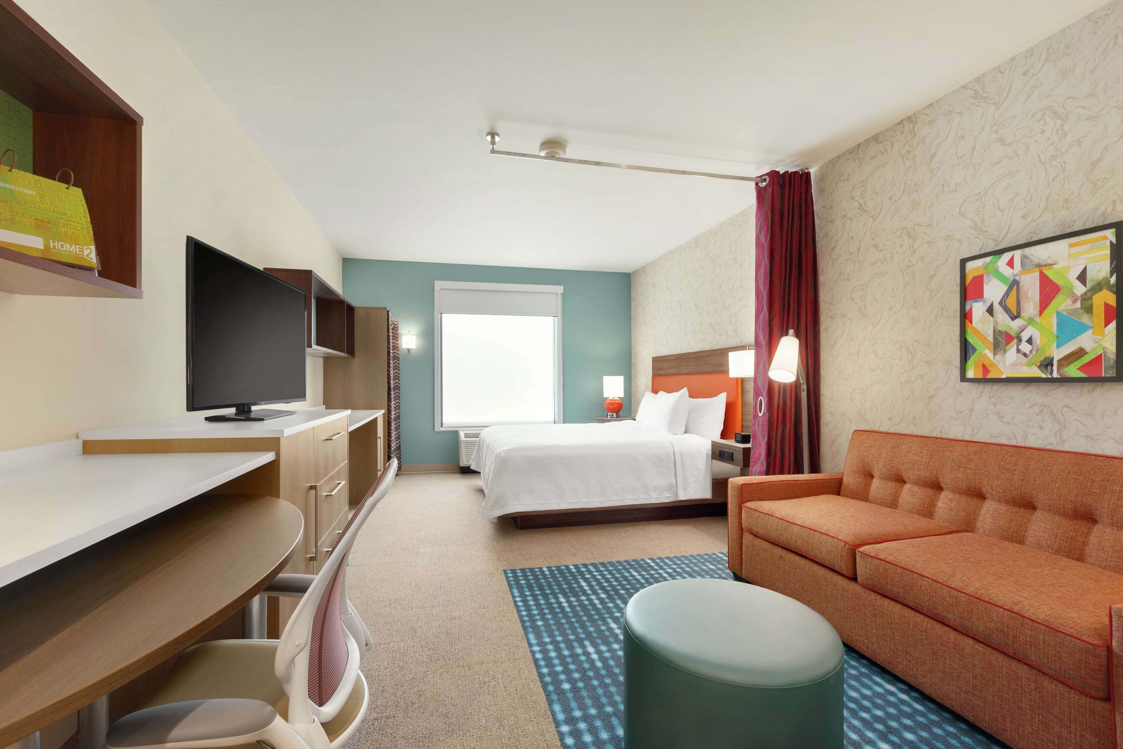 A hotel room with a bed, a desk, a television, a sofa, and a painting on the wall.